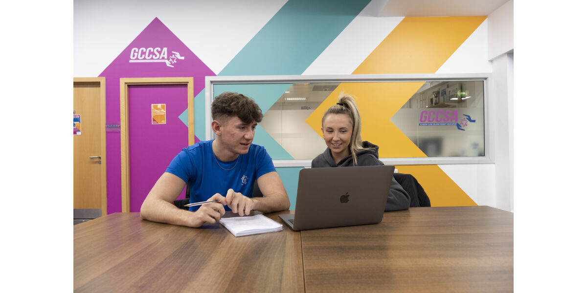 Two students sitting at a table looking at a laptop