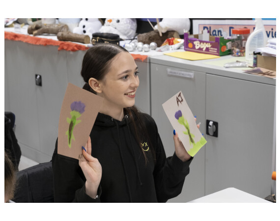 Early Years student holding up two paintings of thistles.